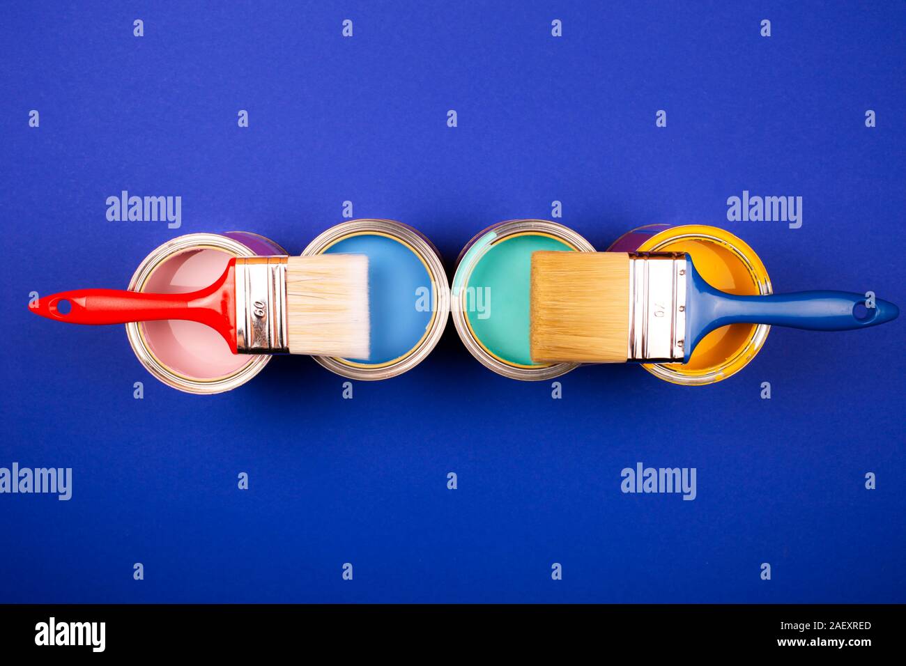 Four open cans of paint with brushes on blue background. Yellow, blue