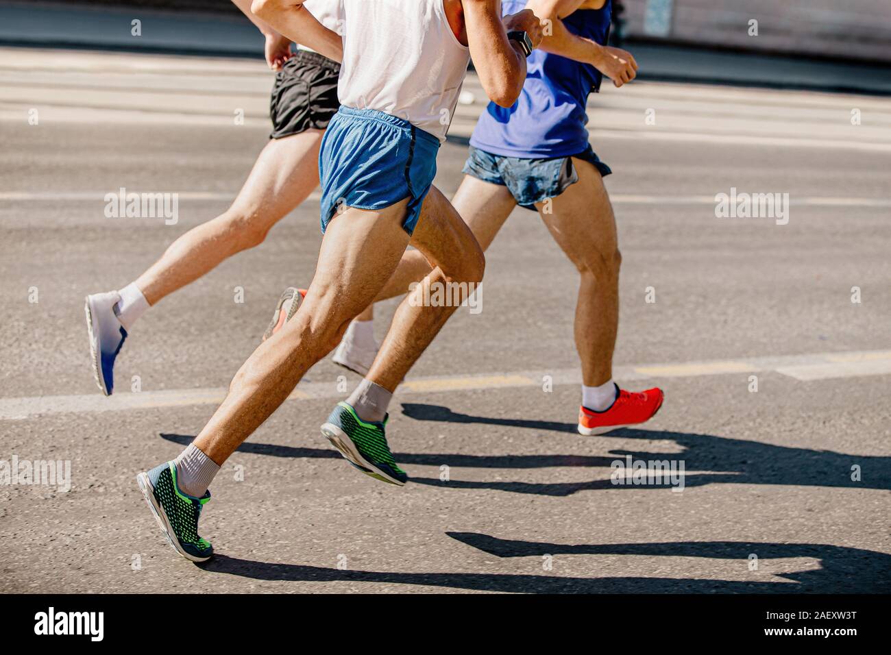 feet three male runners running marathon on gray asphalt Stock Photo