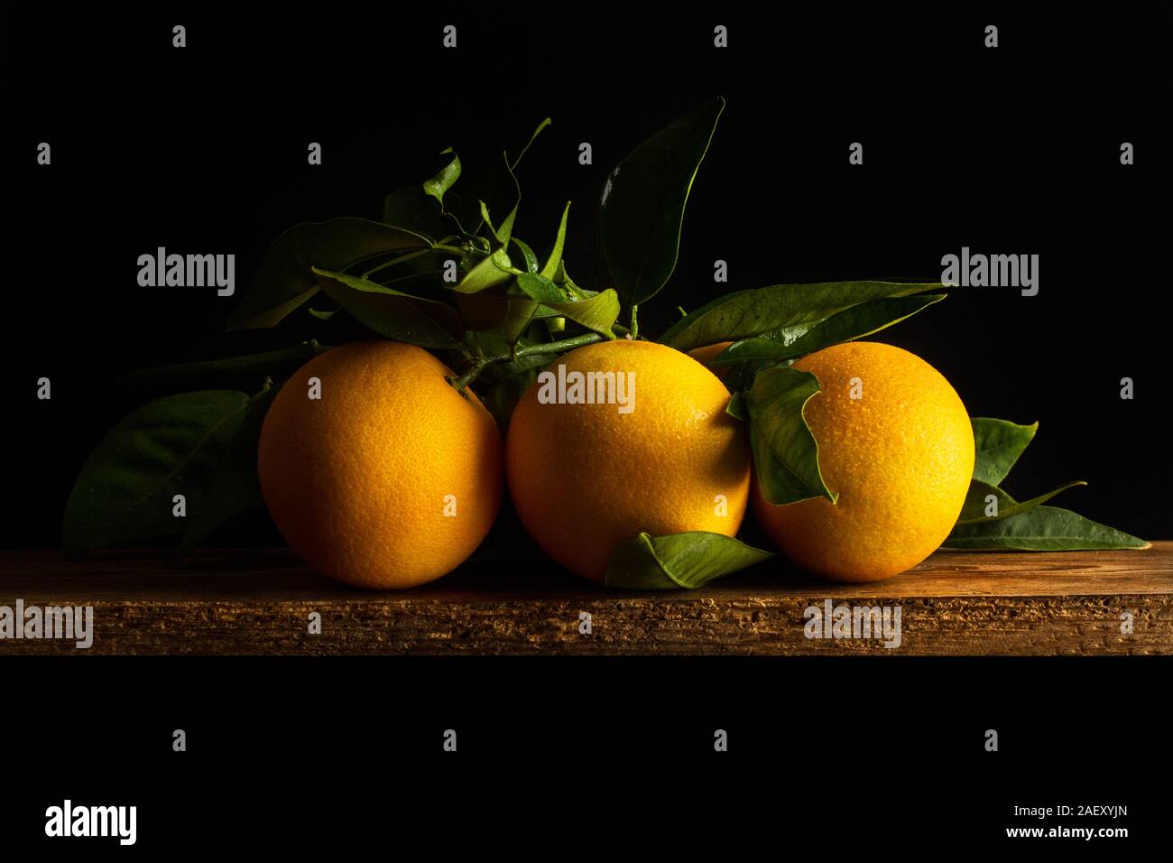 Three oranges with leaves on a wooden table on a dark background Stock Photo