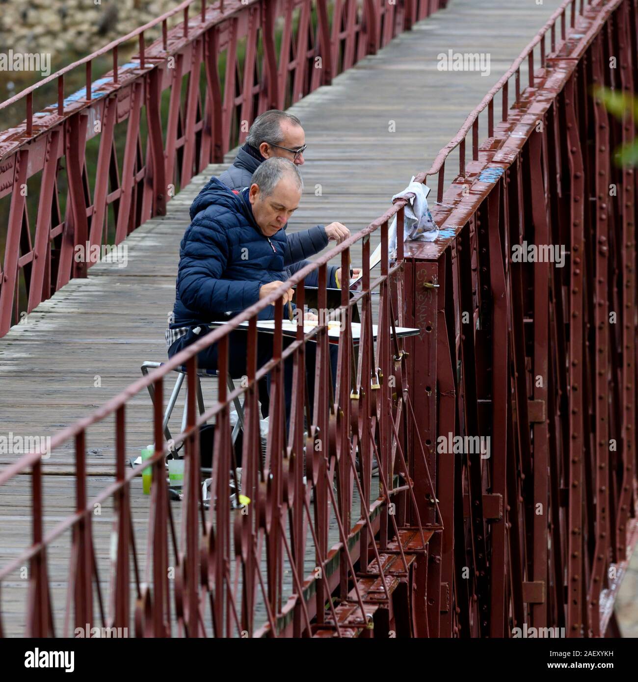 Two senior artists painting on canvas while sitting on San Pablo Bridge, Cuenca, Spain Stock Photo
