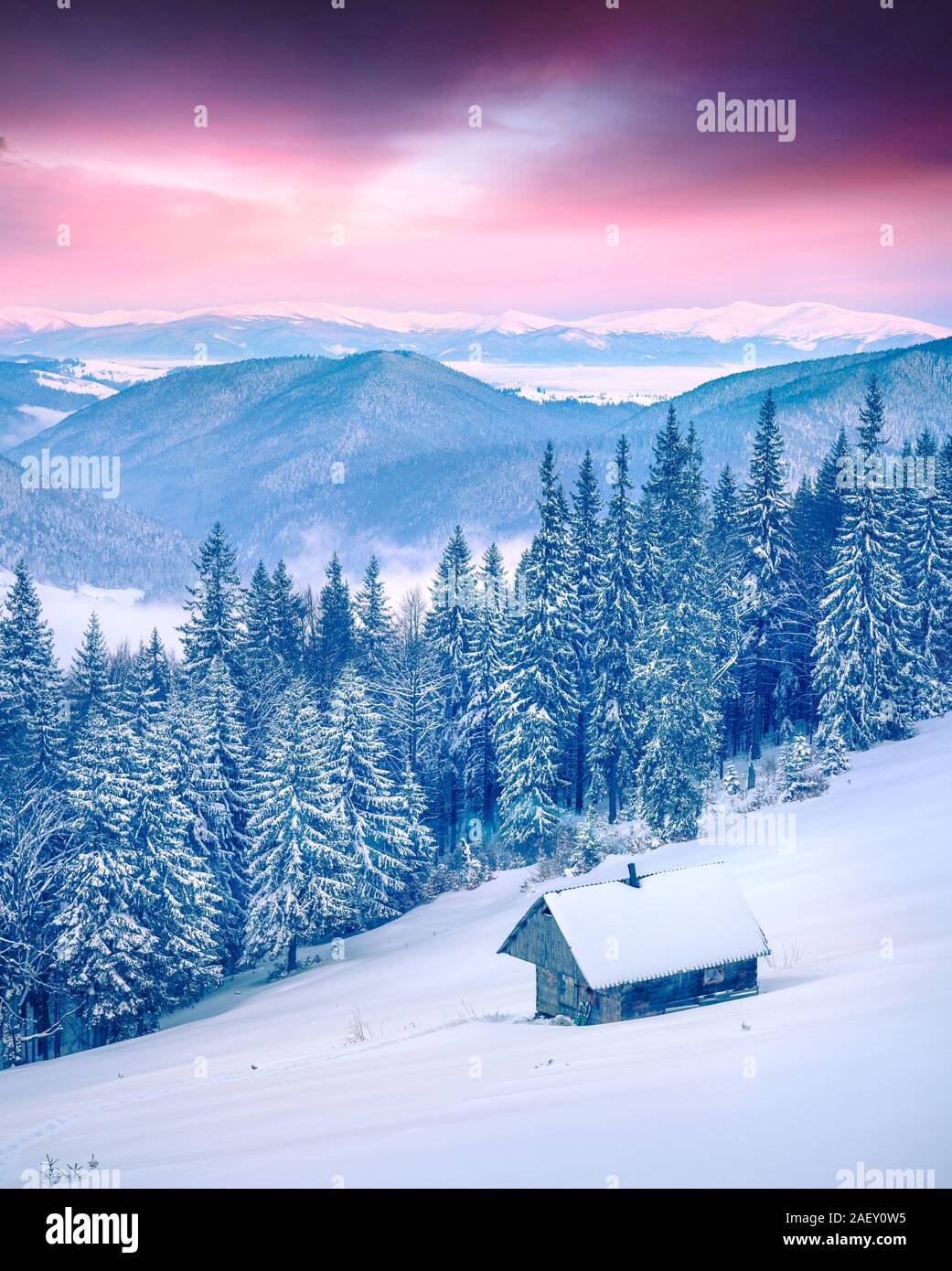 Forester's hut in the snowy mountain forest. Colorful winter sunrise in Carpathians, Happy New Year celebration concept. Stock Photo