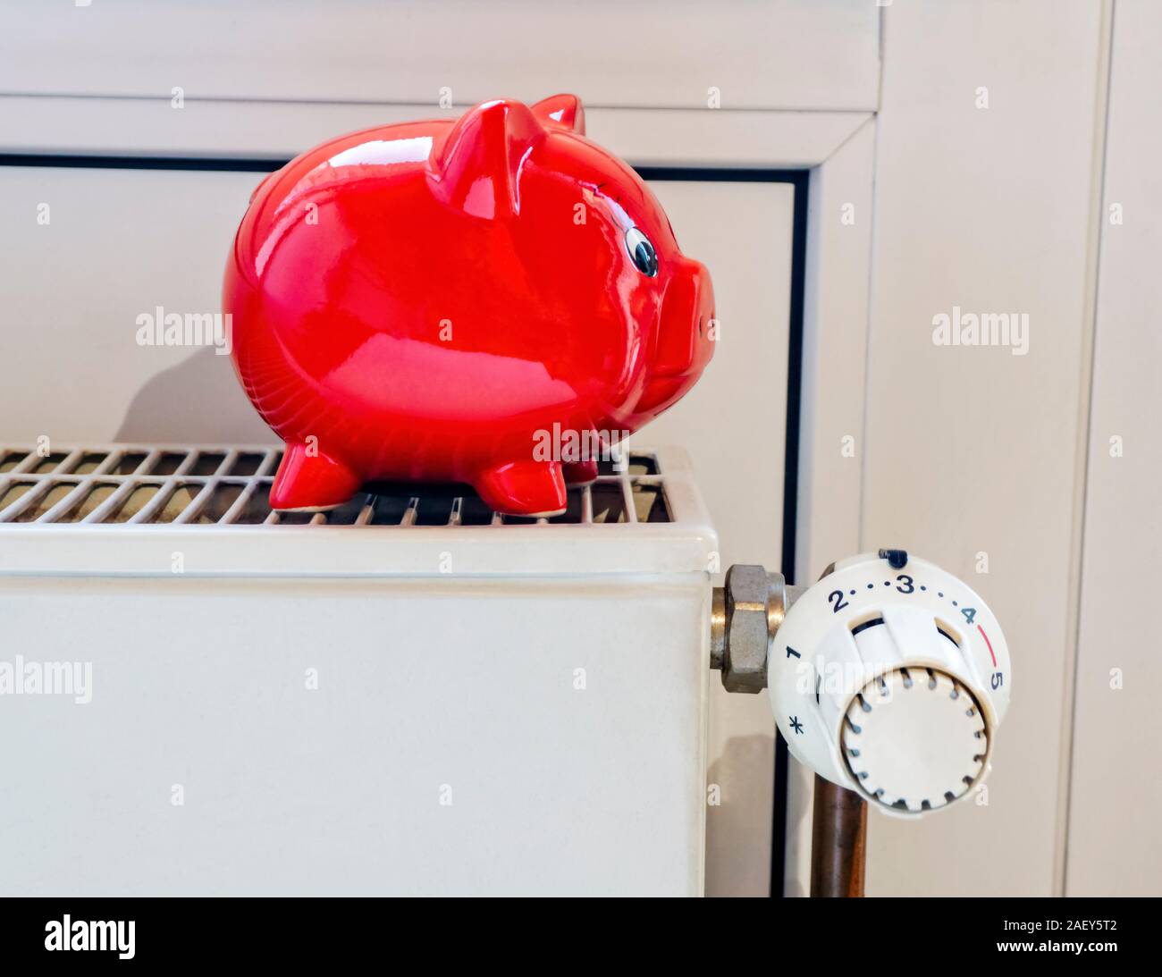 Red piggy bank stands on a heating with thermostat Stock Photo