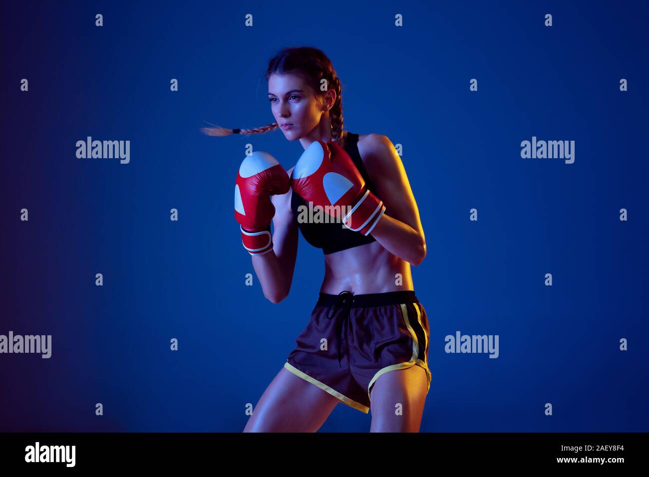Freedom. Fit caucasian woman in sportswear boxing on blue studio background in neon light. Novice female caucasian boxer working out and training. Sport, healthy lifestyle, movement concept. Stock Photo