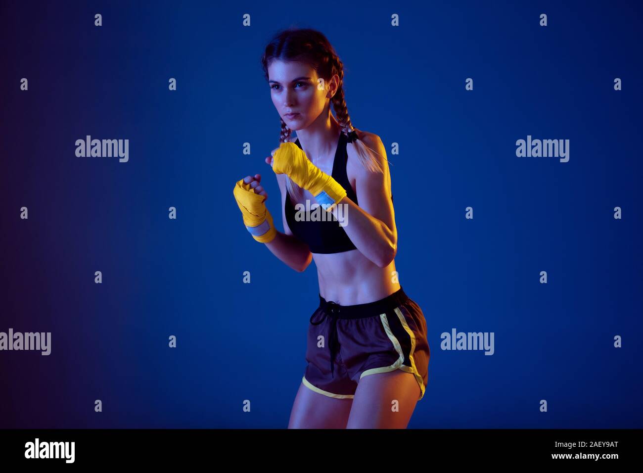 Natural. Fit caucasian woman in sportswear boxing on blue studio background in neon light. Novice female caucasian boxer working out and training. Sport, healthy lifestyle, movement concept. Stock Photo