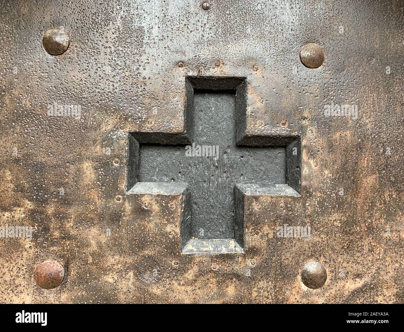 Cutted out black cross in an iron door with rivets, nails and screws. Old metal fitting from the Middle Ages, weathered, oxidized and preserved. Stock Photo