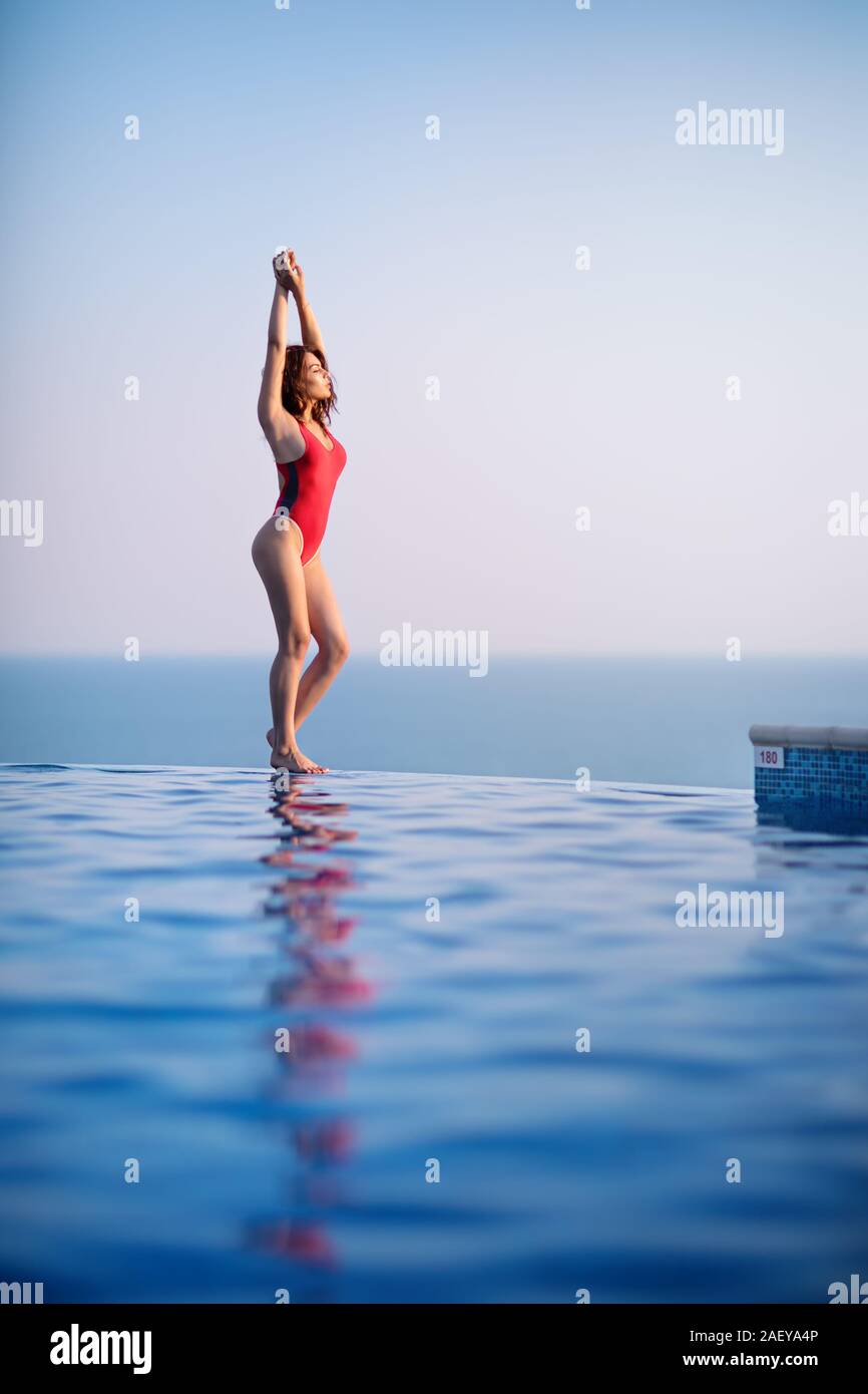 Beautiful young woman in swimsuit at the edge of infinity swimming pool Stock Photo