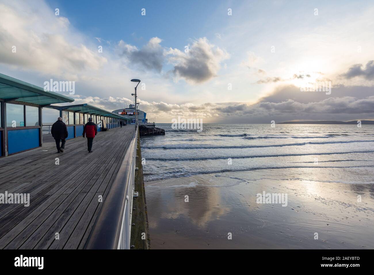 Bournemouth in winter, Dorset, UK, December 2019. Cold with rain showers, sunny with a strong wind on the south coast in the afternoon. Sunshine and stormy clouds over the Isle of Purbeck and hardy people on the pier in winter coats. Stock Photo
