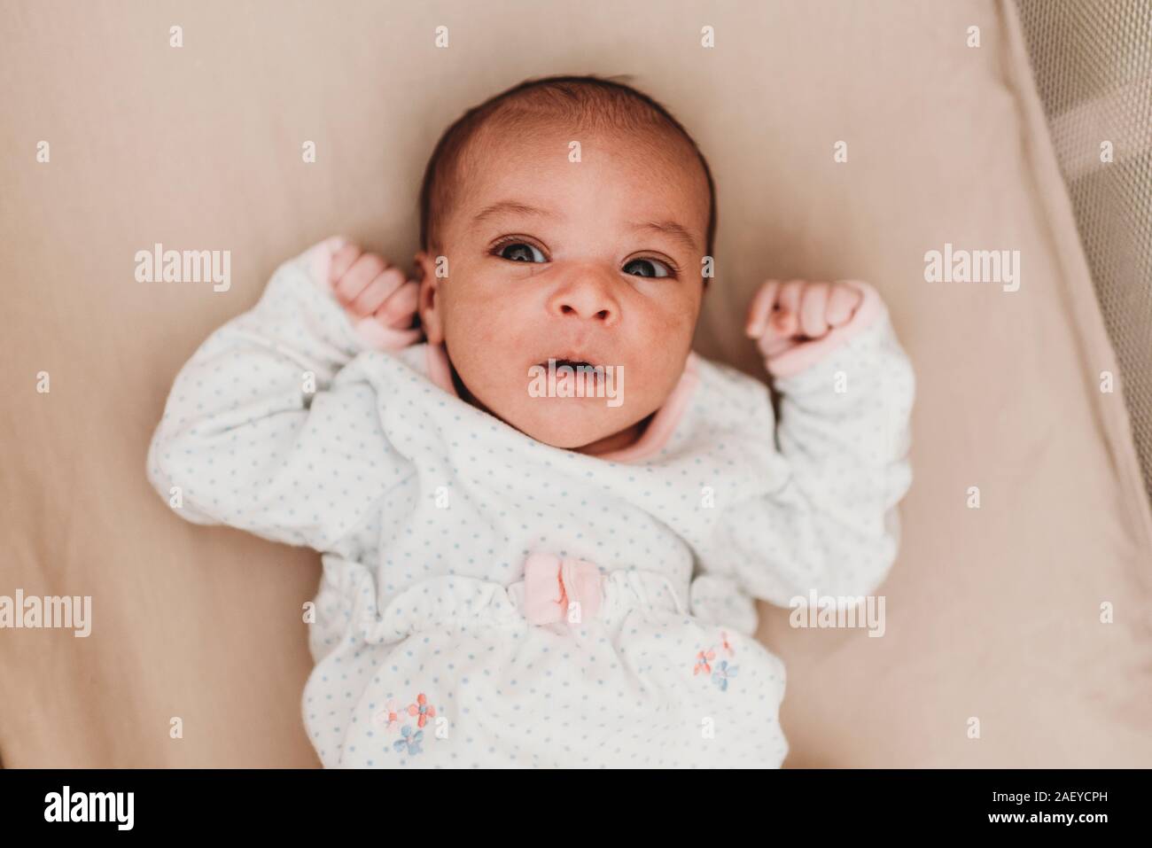 Dark-haired month old baby with wide open eyes lying in crib Stock Photo