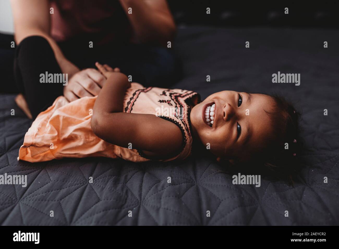 Sweet multiracial 2 yr old girl lying on bed laughing Stock Photo
