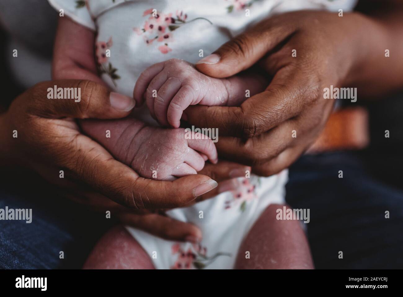 Ethnic female hands holding tiny waxy hands of multiracial newborn Stock Photo