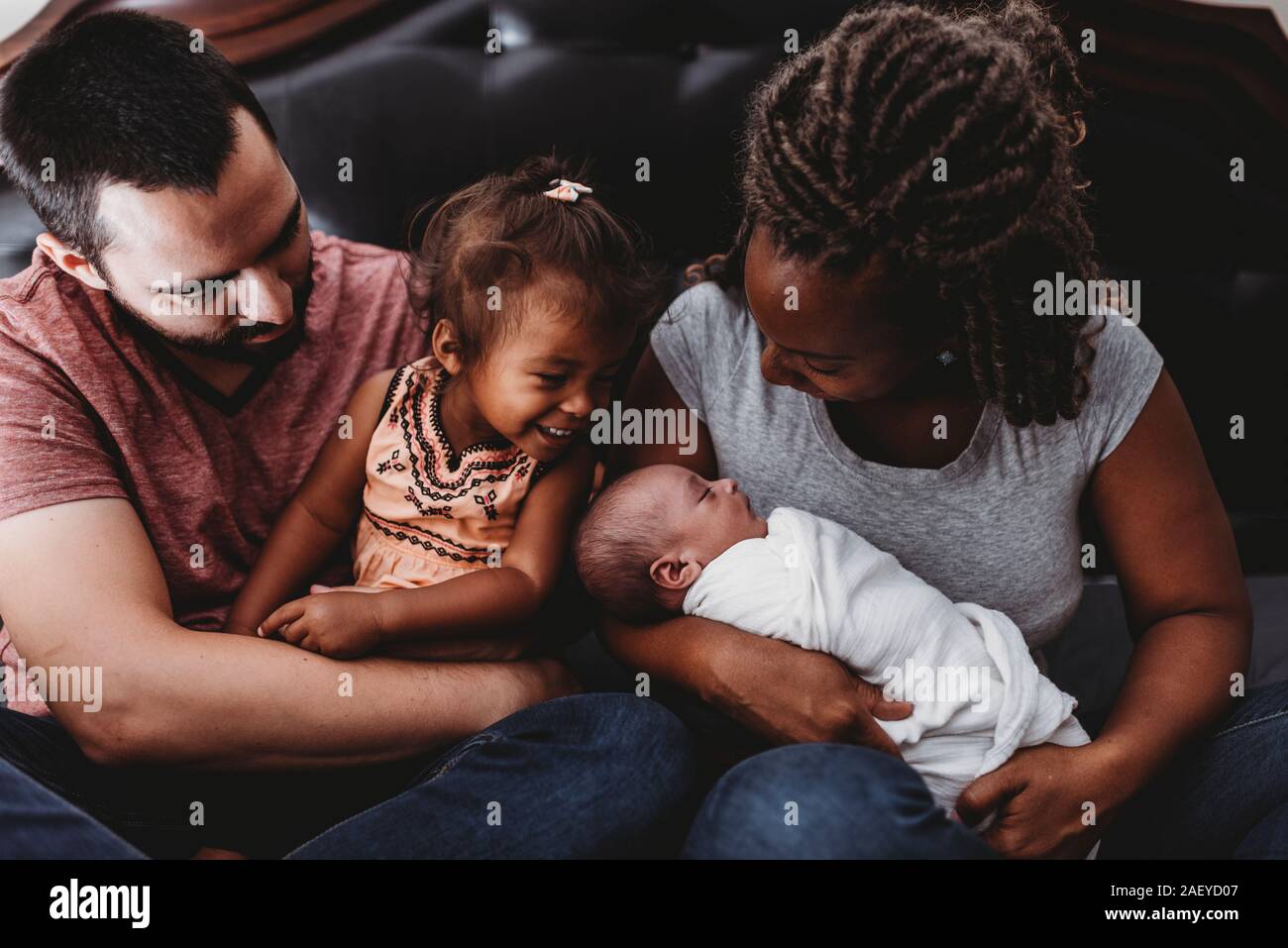 Multiracial parents holding smiling 2 yr old girl and swaddled baby Stock Photo