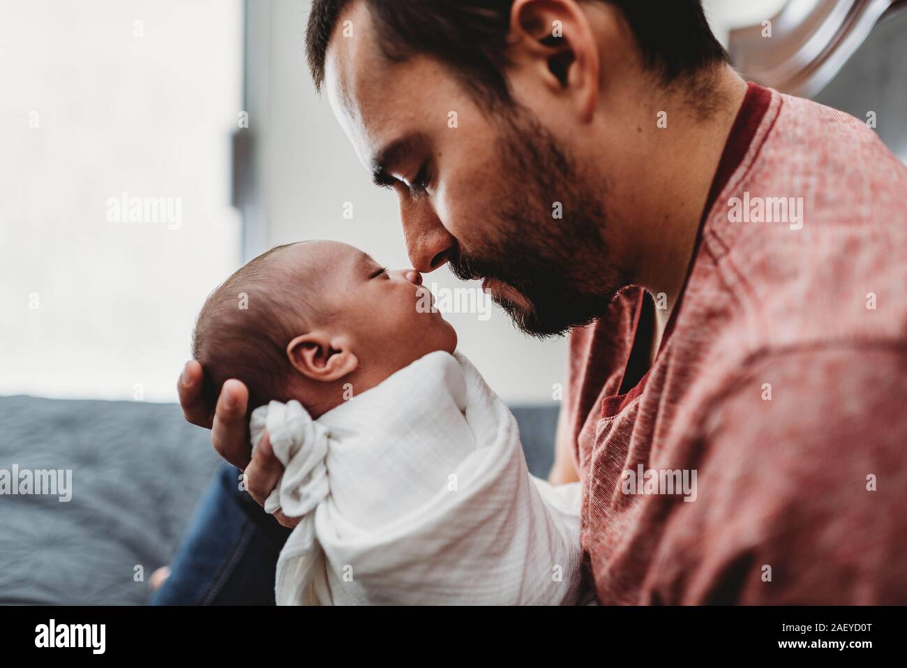 Olive-skinned dad with beard touches nose to swaddled newborn Stock Photo