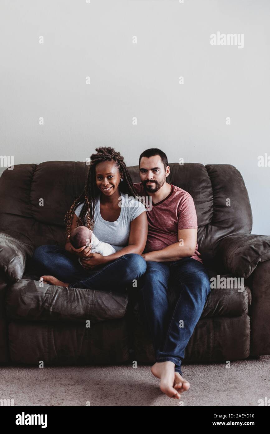 Multiracial couple holding swaddled newborn while sitting on couch Stock Photo