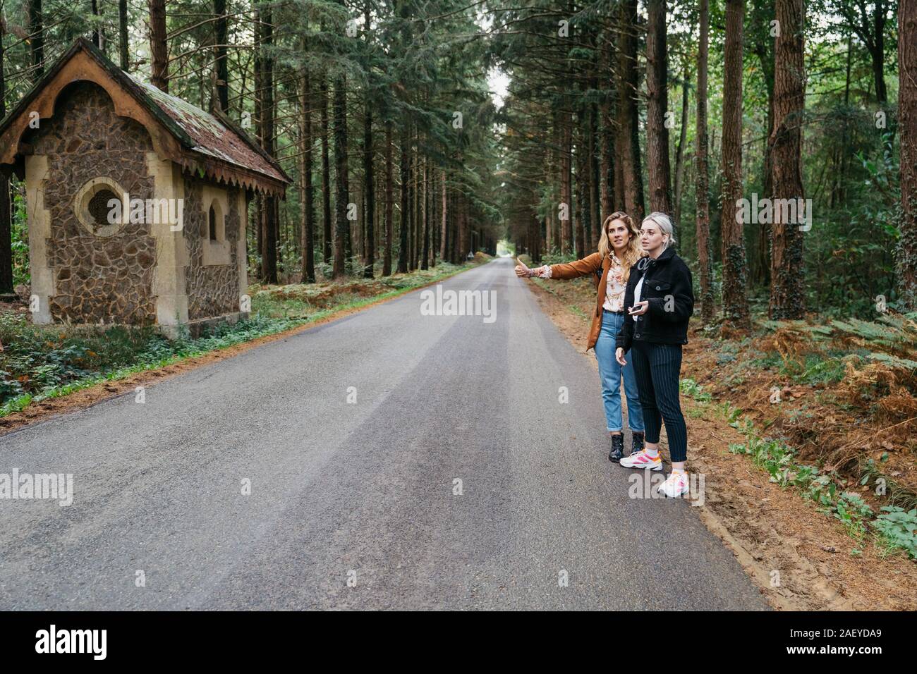 Two women hitchhiking on a forest road in France Stock Photo