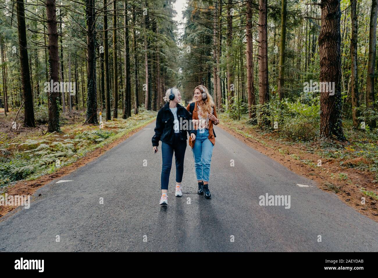 Two women walking on a road in the forest while listening to music Stock Photo