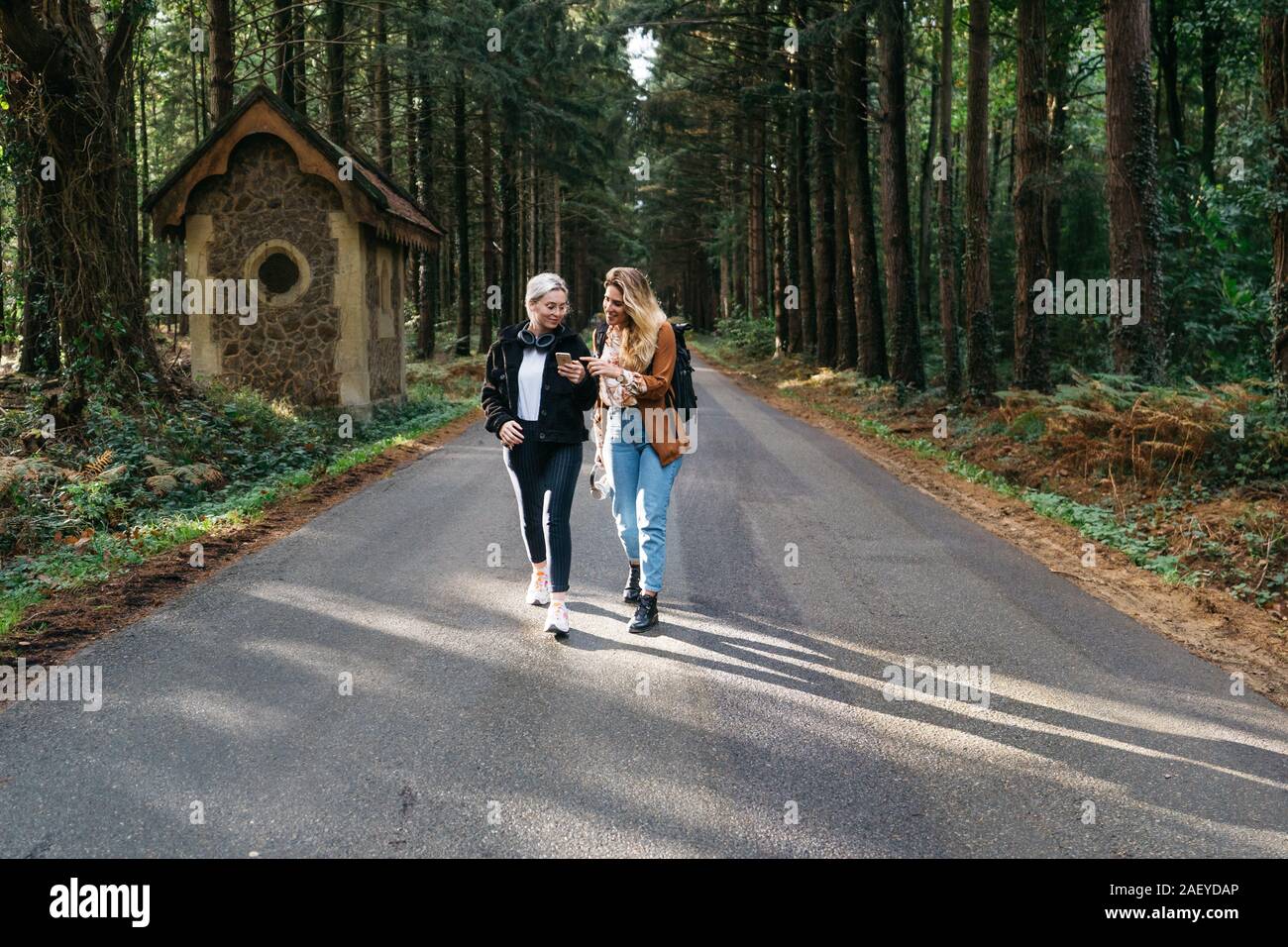 Two women walking down the road looking at their phone Stock Photo