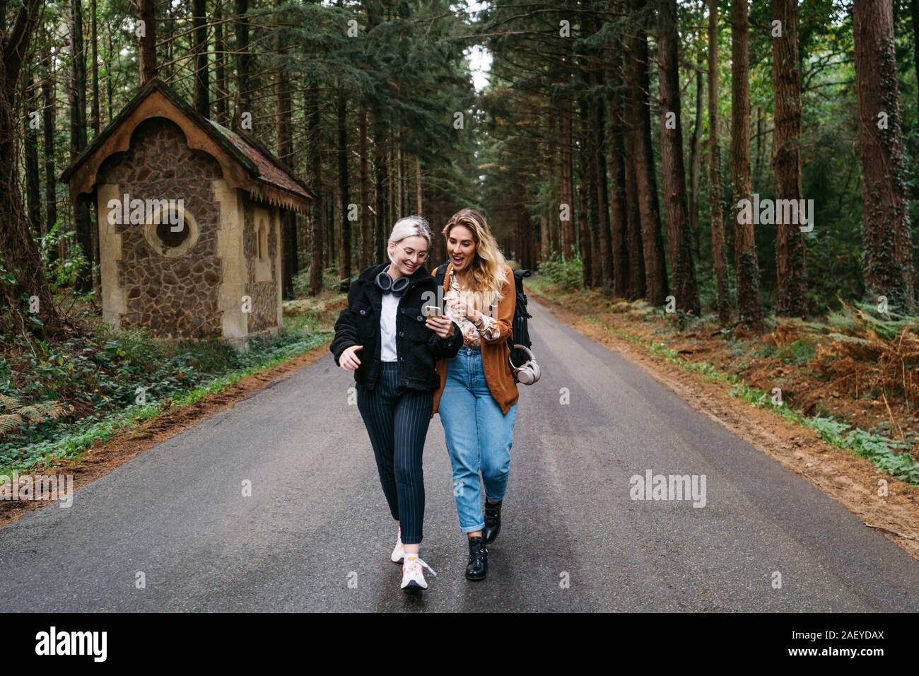 Two women walking down the road looking at their phone and laughing Stock Photo