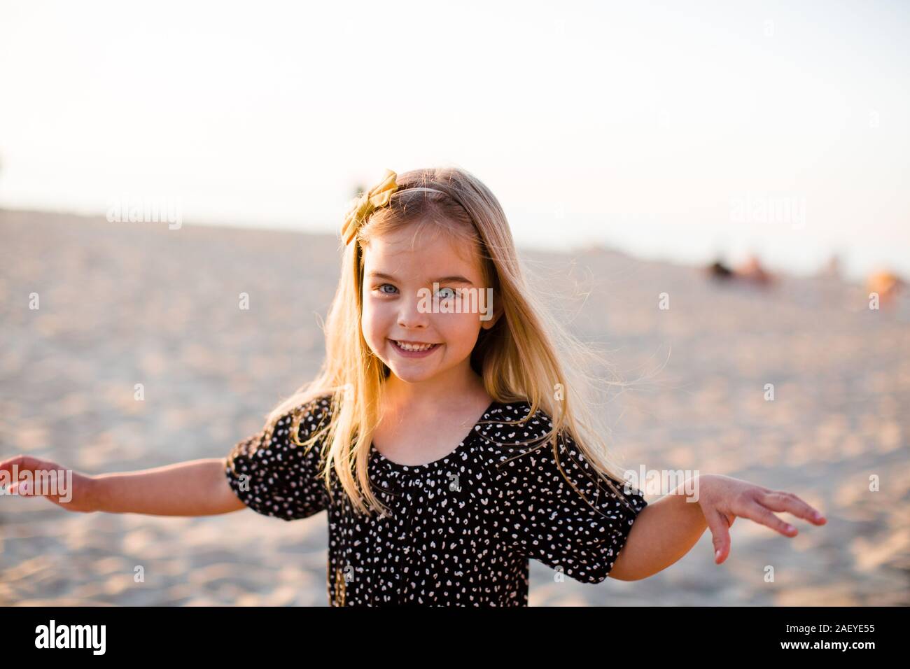 Young Girl Playing on Beach, Smiling at Camera at Sunset Stock Photo