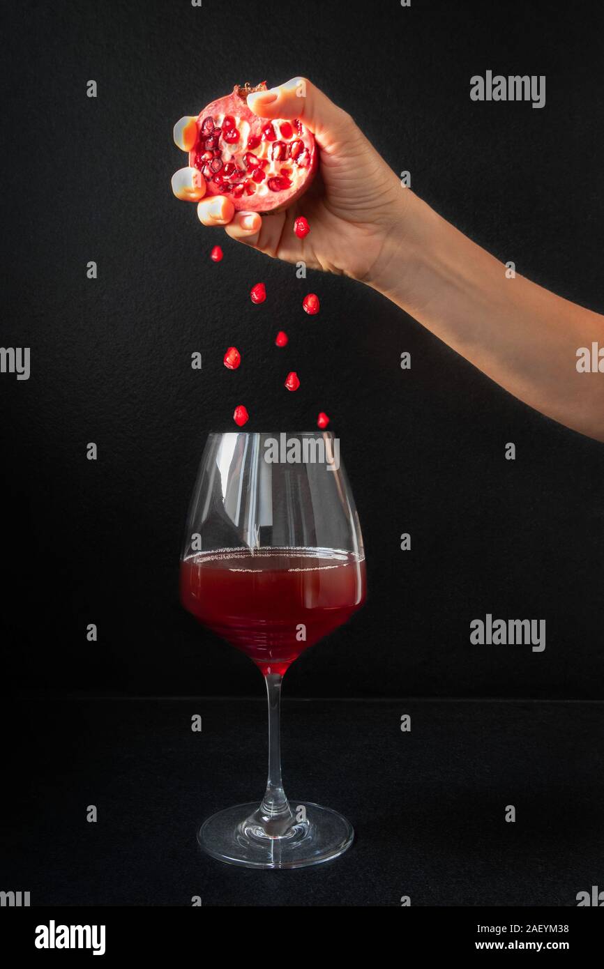 Woman hand holding sliced pomegranate and seeds falling into glass of pomegranate wine Stock Photo
