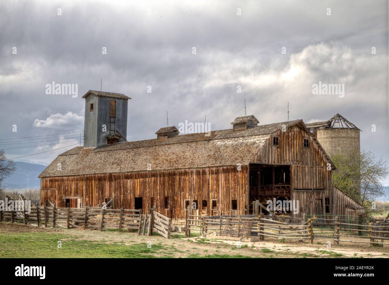 A rustic barn surrounded by an equally weather worn wood fence and accompanied by a roofless silo. Stock Photo