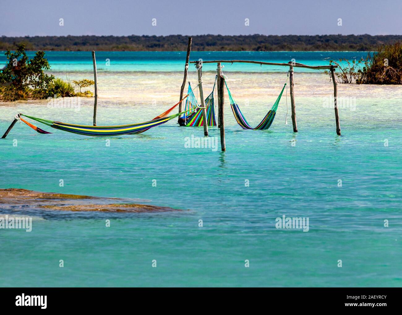 Hammocks hang over the pristine, azure water on Bacalar Lake near the Cocalitos formations, Quintana Roo, Mexico. Stock Photo