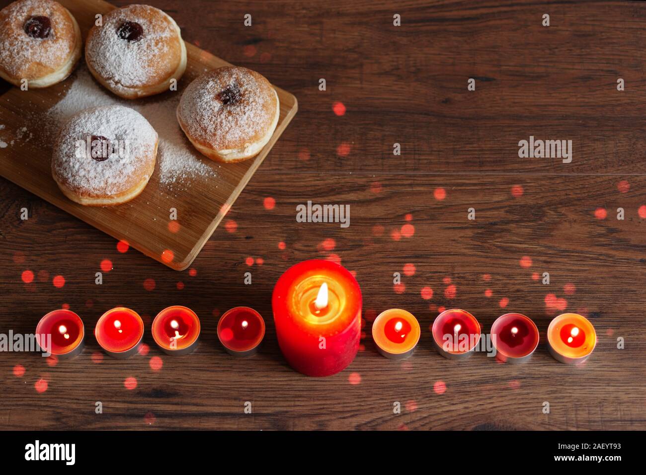 Menorah with candles (traditional Candelabra) and traditional donuts sufganiyot on wooden table for Hanukkah celebration. Stock Photo