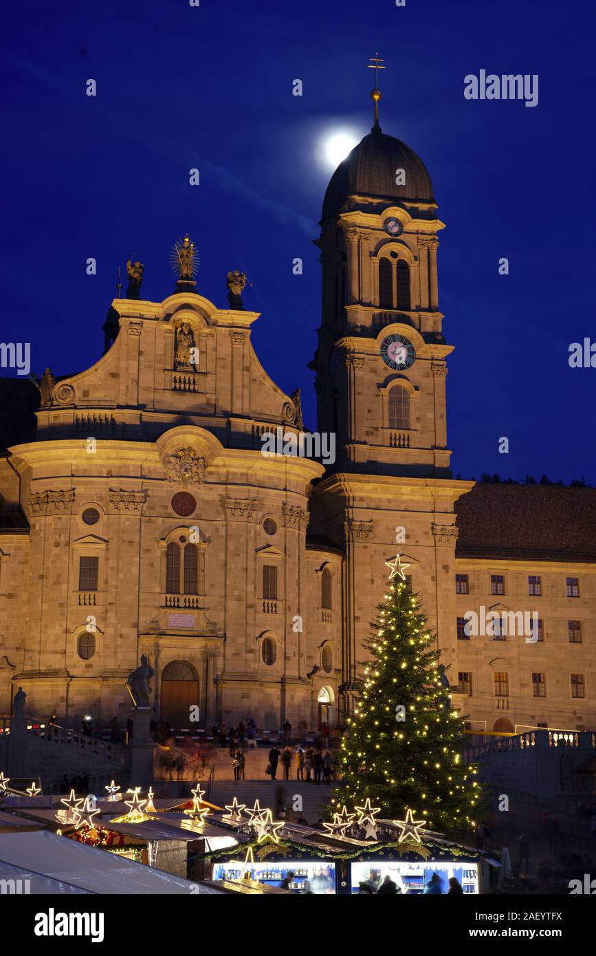 Einsiedler Weihnachtsmarkt (Christmas market) in front of the monastery Einsiedeln at dawn with a christmas tree, booths and the moon shining above. Stock Photo