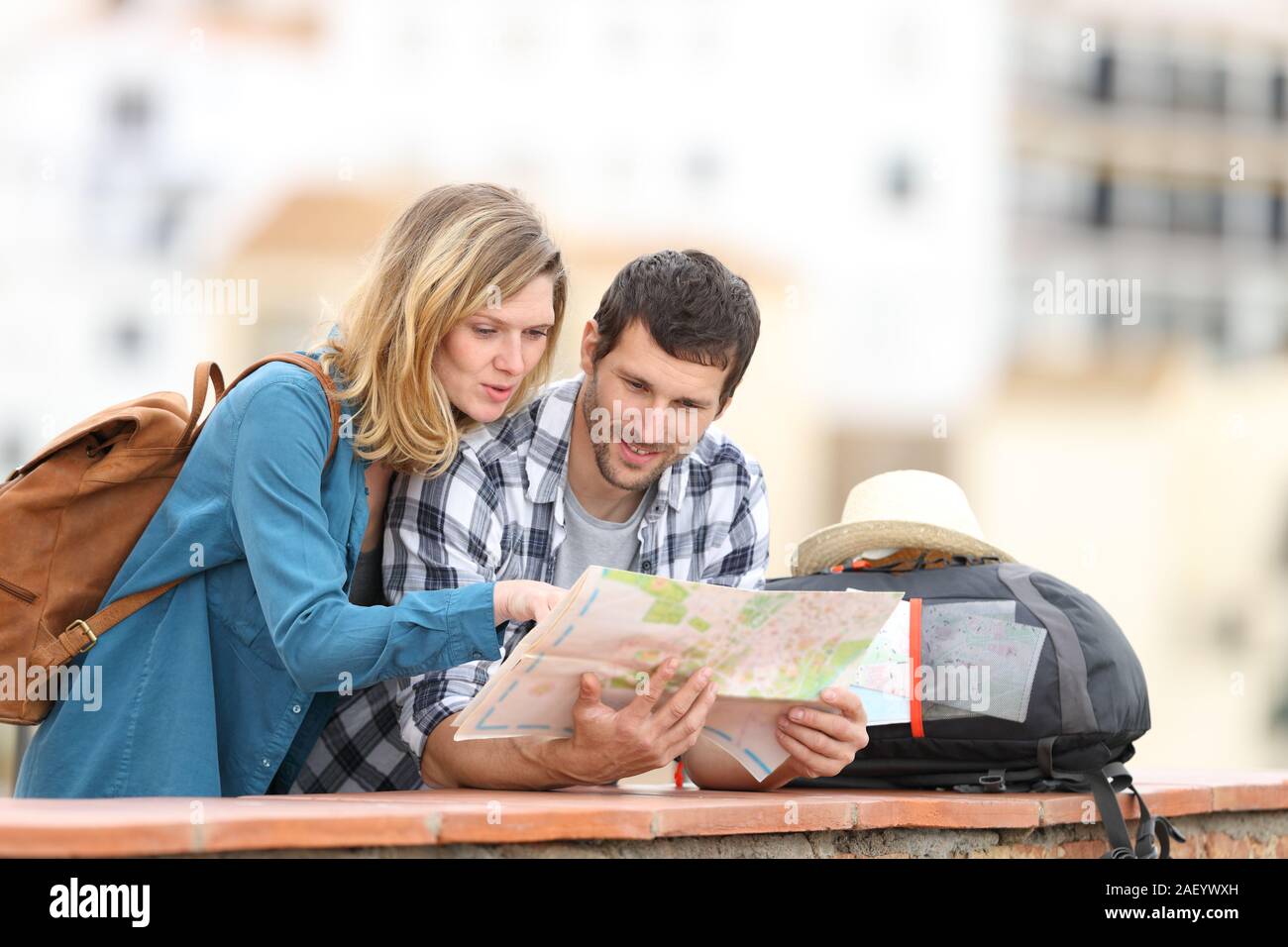 Couple of tourists talking checking paper map on vacation standing outdoors in a balcony in a rural town Stock Photo