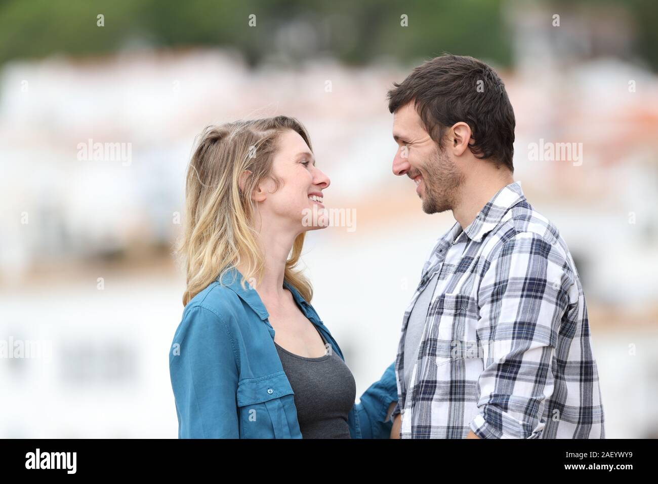 Profile of a couple flirting looking each other standing outdoors in a rural town Stock Photo