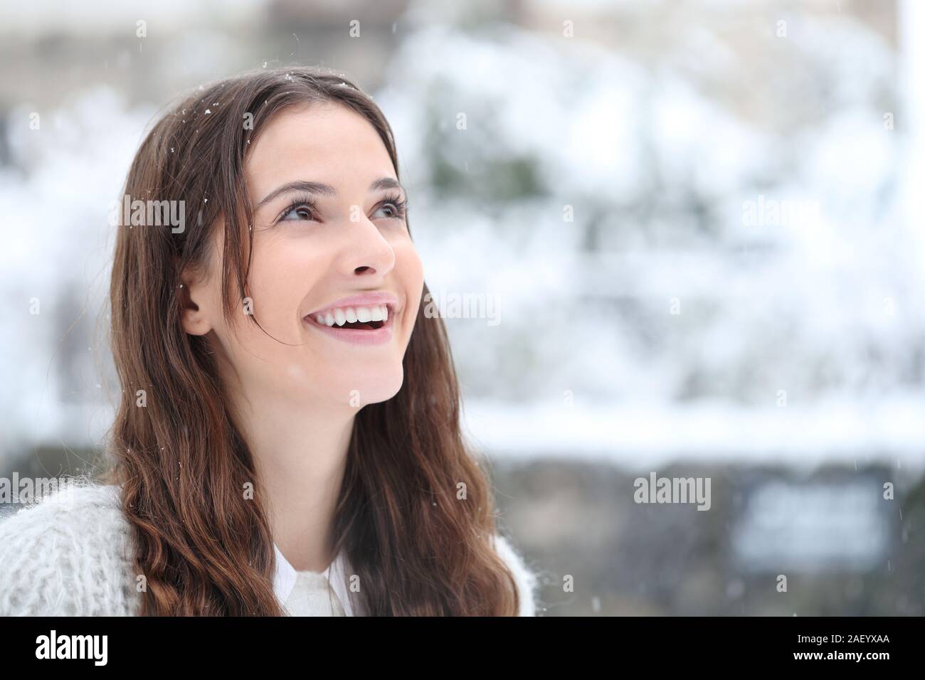 Portrait of a candid happy girl looking how snow is falling in winter Stock Photo