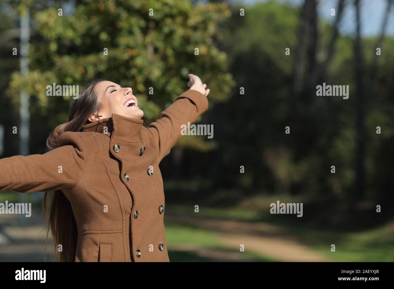 Excited woman wearing jacket outstretching arms in a park in winter Stock Photo