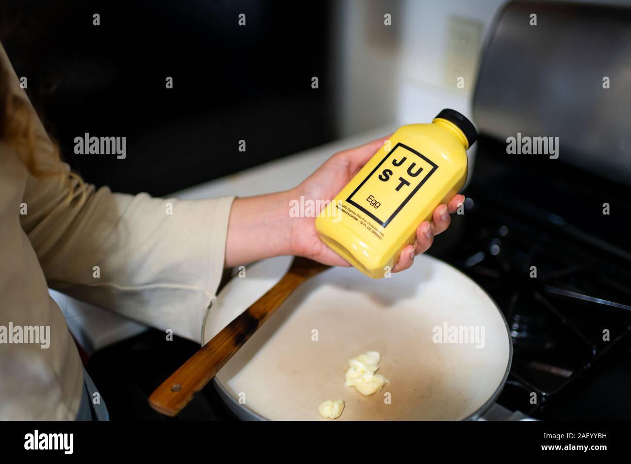 Aspen, USA - September 20, 2019: Woman holding Just Egg replacement for scrambled omelette in hand by ceramic frying pan with butter Stock Photo