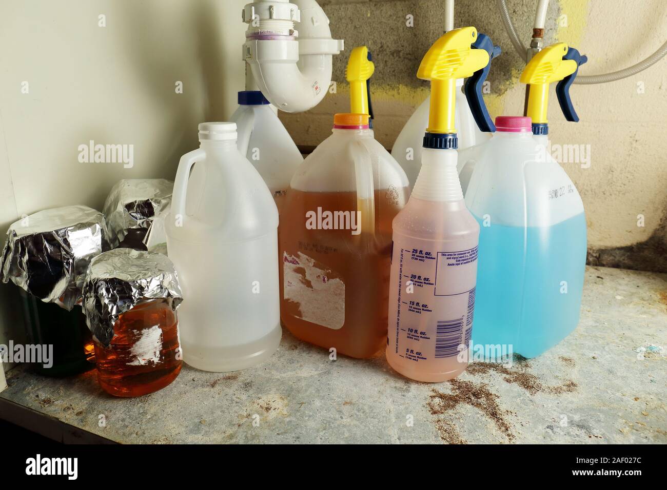 Variety in mysterious chemicals stored improperly in jugs, jars, and spray bottles under a sink Stock Photo