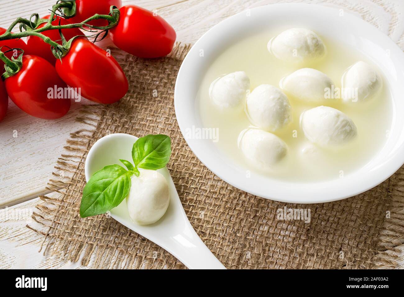 Brine with mini mozzarella cheese balls in a bowl, one mozzarella ball and basil in a spoon and