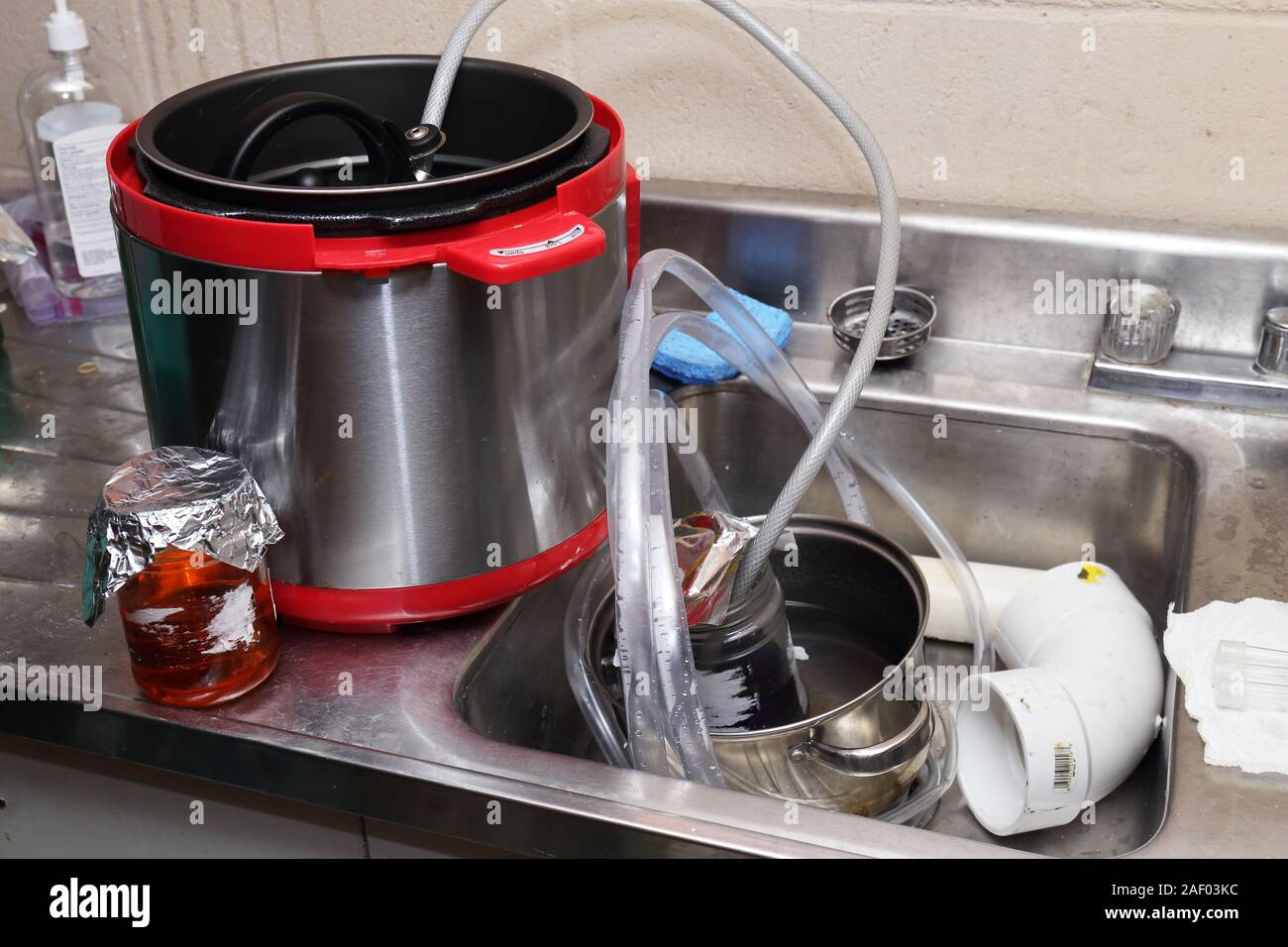 Homemade synthesis of a chemical, most likely something illegal, in a basement sink using a pressure cooker, hoses, and a jar in a pot of water to con Stock Photo