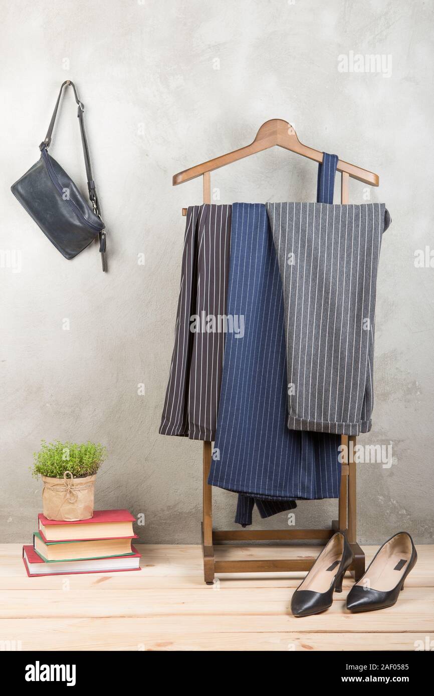 Shopping and style concept - clothes rack with trendy striped pants, blue bag and shoes on wooden floor and grey concrete background. Vertical photo Stock Photo