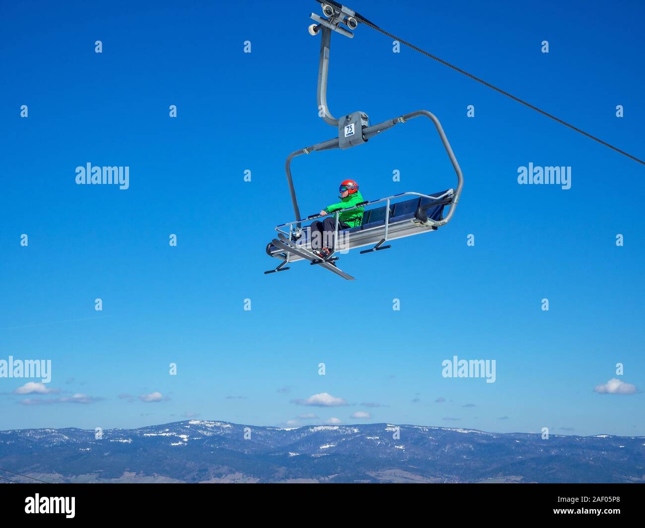 Bialka Tatrzanska, Poland - March 27, 2018: A Chairlift for skiers and snowboarders with a skier in a green ski jacket, red helmet and goggles on blue Stock Photo