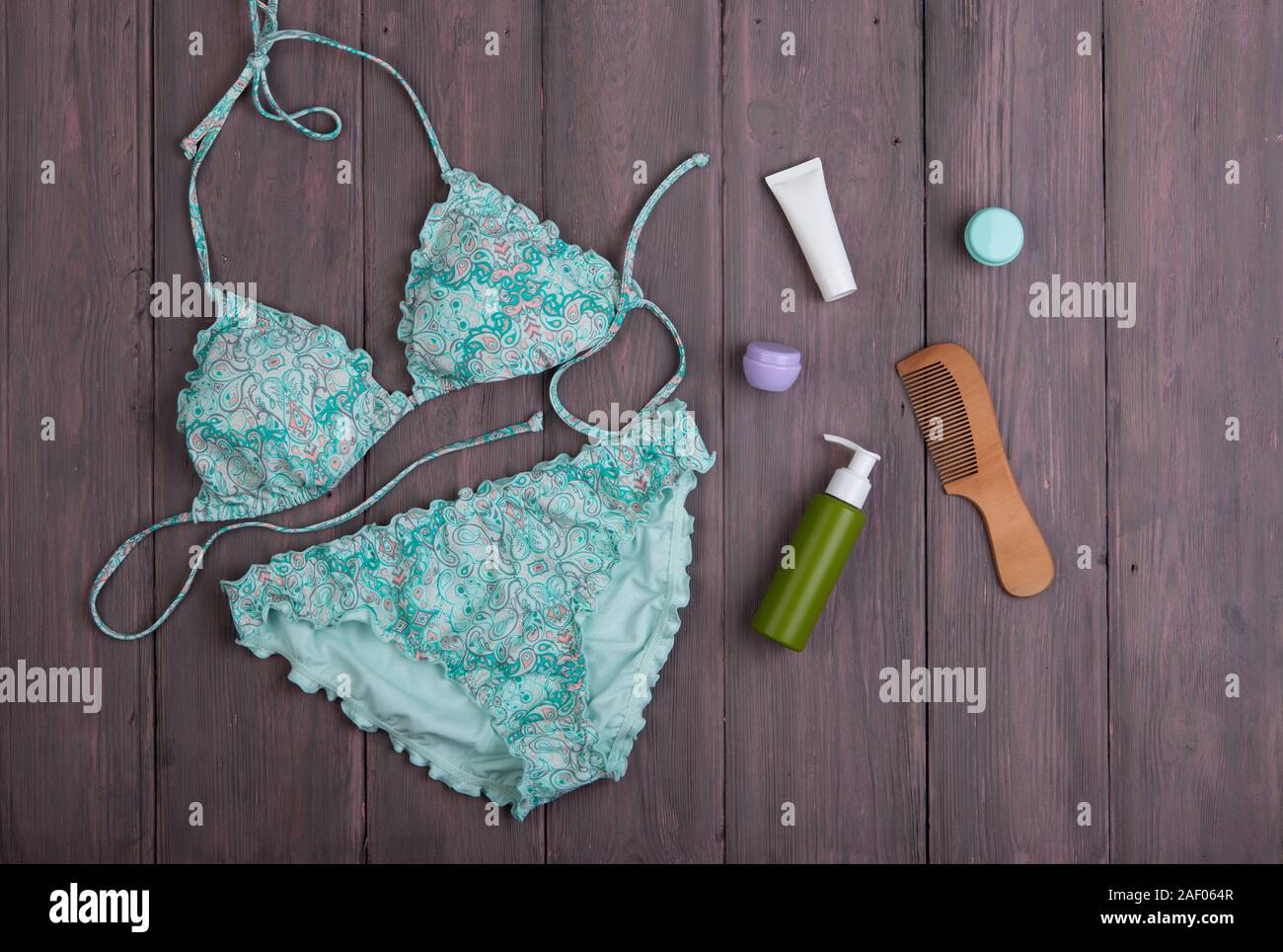 Sea holidays / travel concept - blue beautiful swimsuit and accessories: wooden hairbrush, sunscreen, bottles with cream on wooden background Stock Photo
