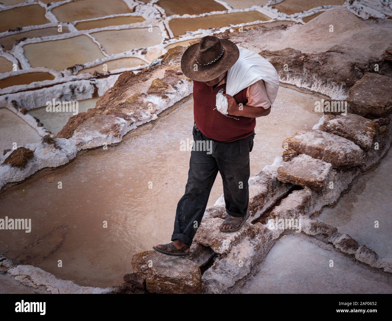 MARAS, PERU - CIRCA SEPTEMBER 2019:  Worker carrying a bags at the Marasal salt mines near the village of Maras in the Cusco region known as Sacred Va Stock Photo