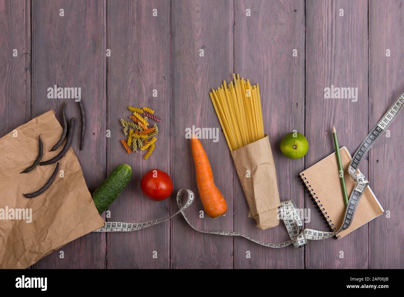 Diet food diary - notebook to count calories, centimeter tape, fresh vegetables in eco paper bag, spaghetti pasta on wooden table Stock Photo