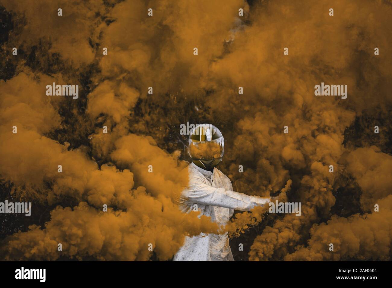 guy in mask standing in between orange brown smoke bombs Stock Photo