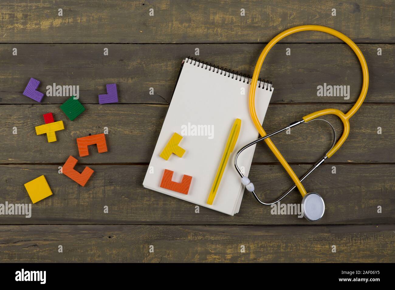 Children's healthy development concept - blank notepad, yellow stethoscope, colorful wooden jigsaw puzzles on wooden background Stock Photo