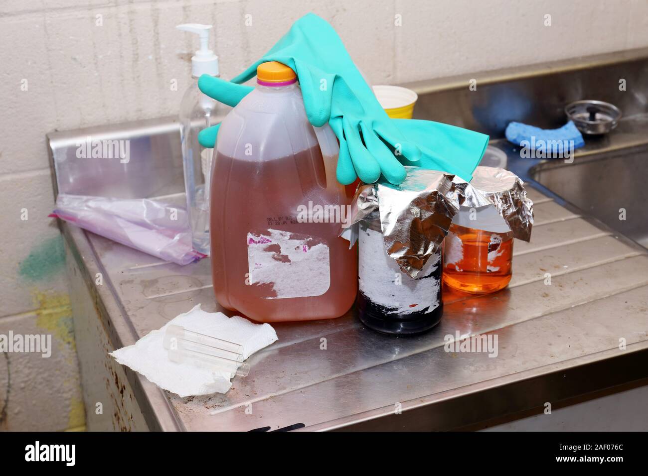 Unlabeled chemicals with gloves resting on top on a steel counter top next to a sink Stock Photo
