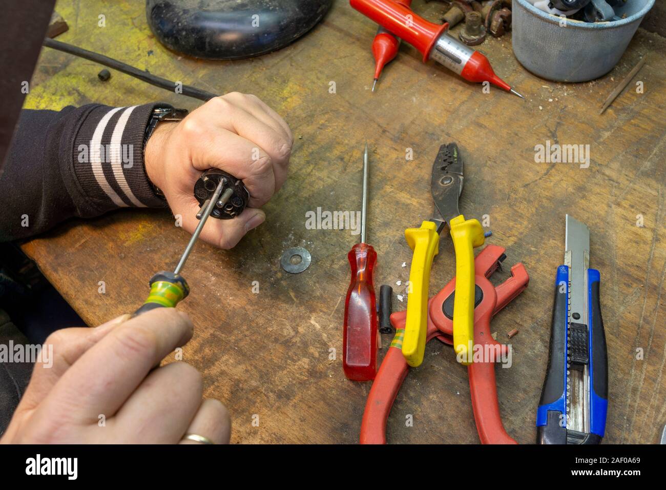 Electrician repairs a cable, there are tools on his workbench. Stock Photo