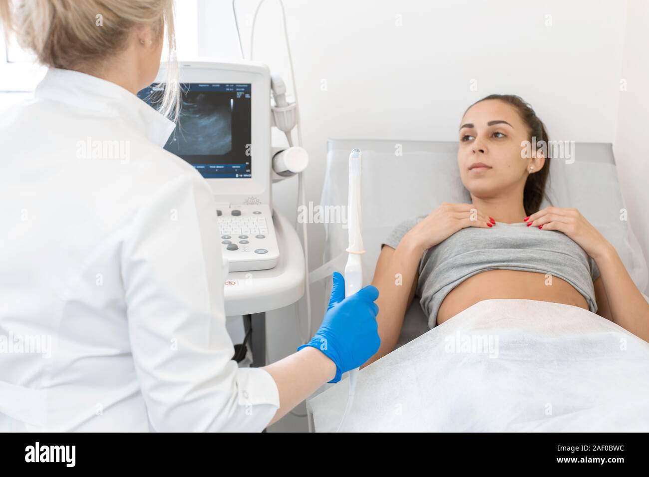 A Gynecologist Sets Up An Ultrasound Machine To Diagnose A Patient Who Is Lying On A Couch A 