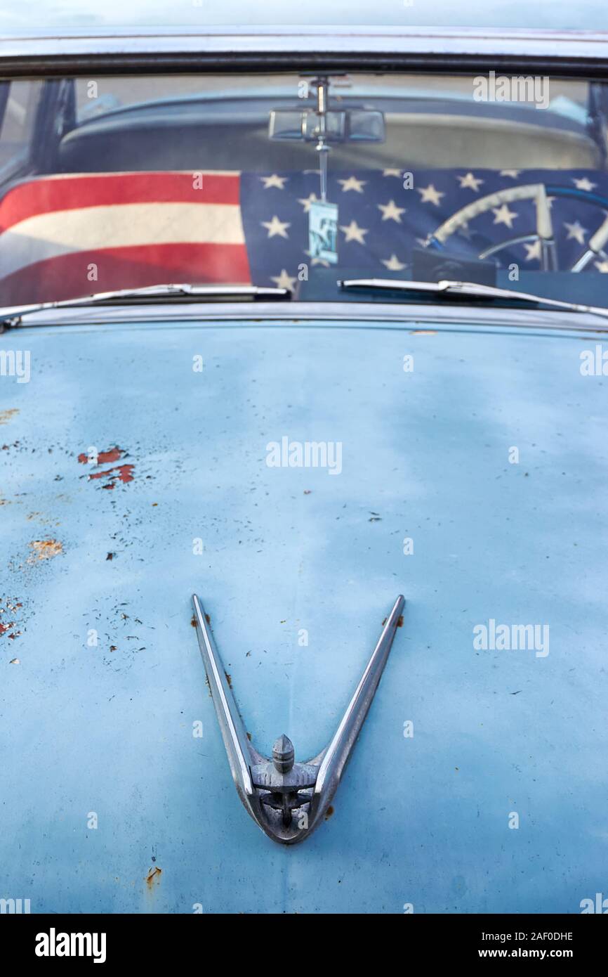 Hood and windscreen of an old blue, weathered rusty old timer vintage car with v shaped hood ornament with head and american flag covering the seat Stock Photo
