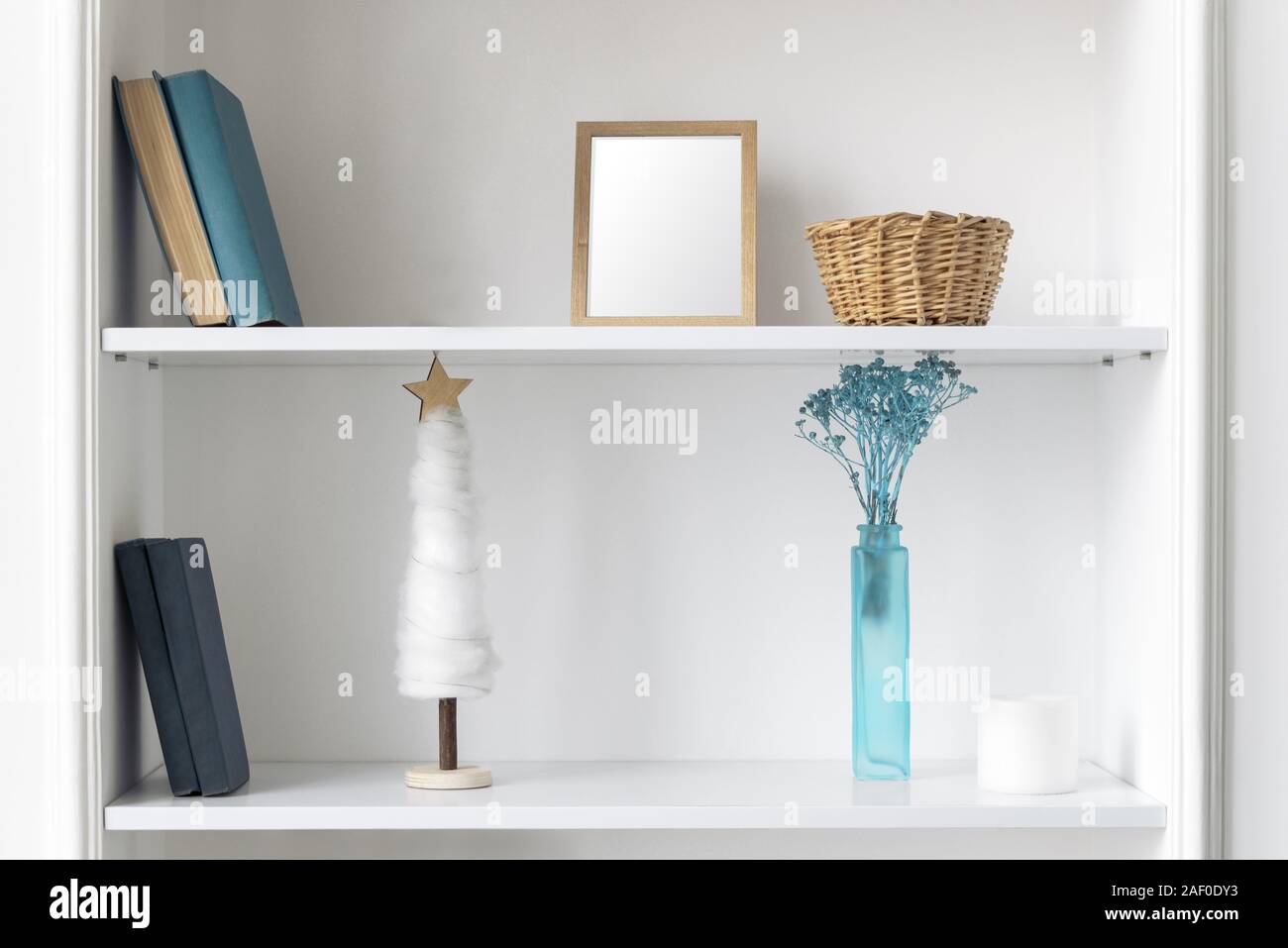 Blue vase, frame and books on white shelves. Classic blue Home accessories and books on wall shelves. Stock Photo