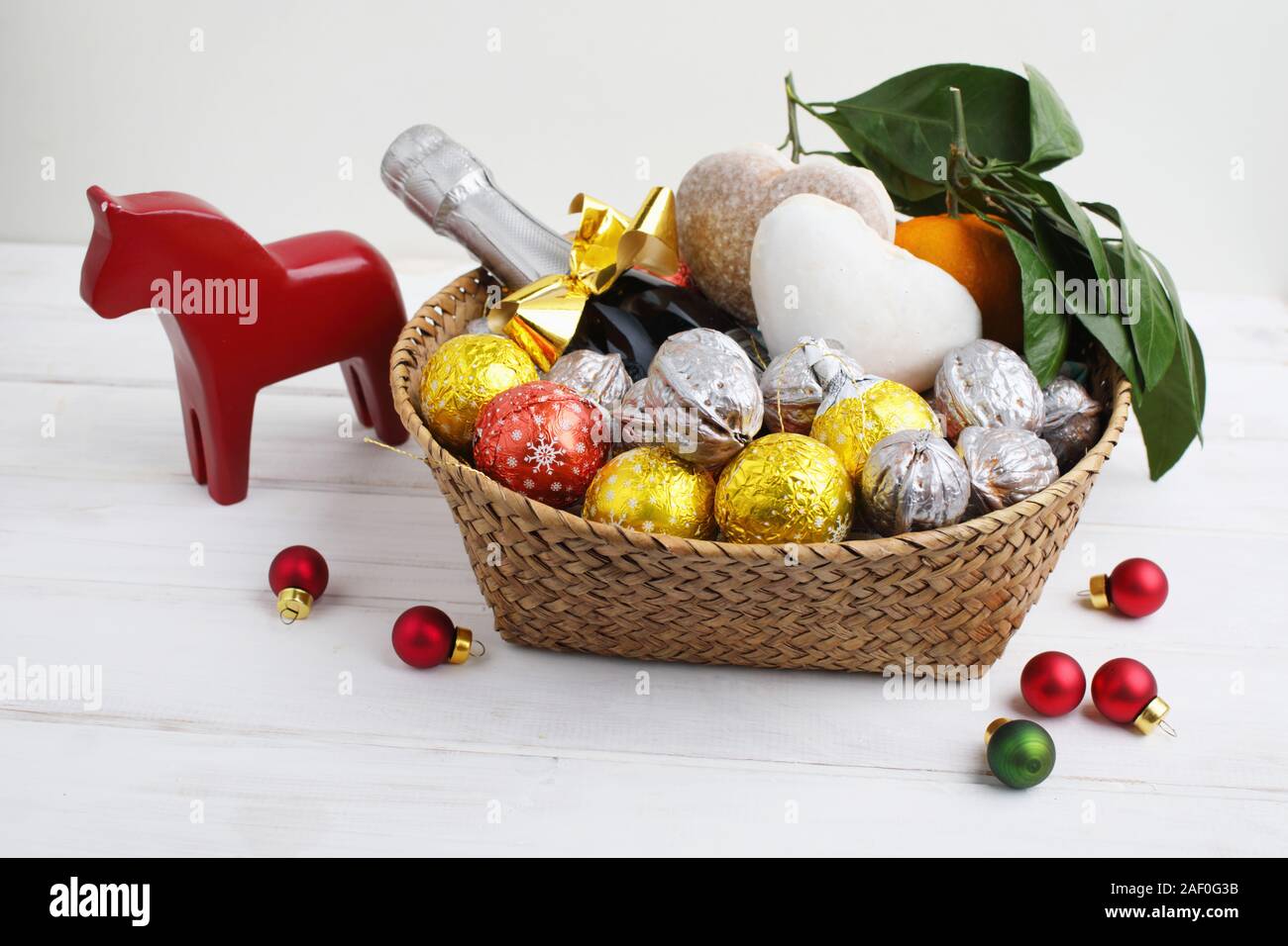 Christmas gift basket with chocolate candies, walnuts, gingerbread, mandarin oranges, a bottle of champagne, and a statue of Swedish Dala horse Stock Photo