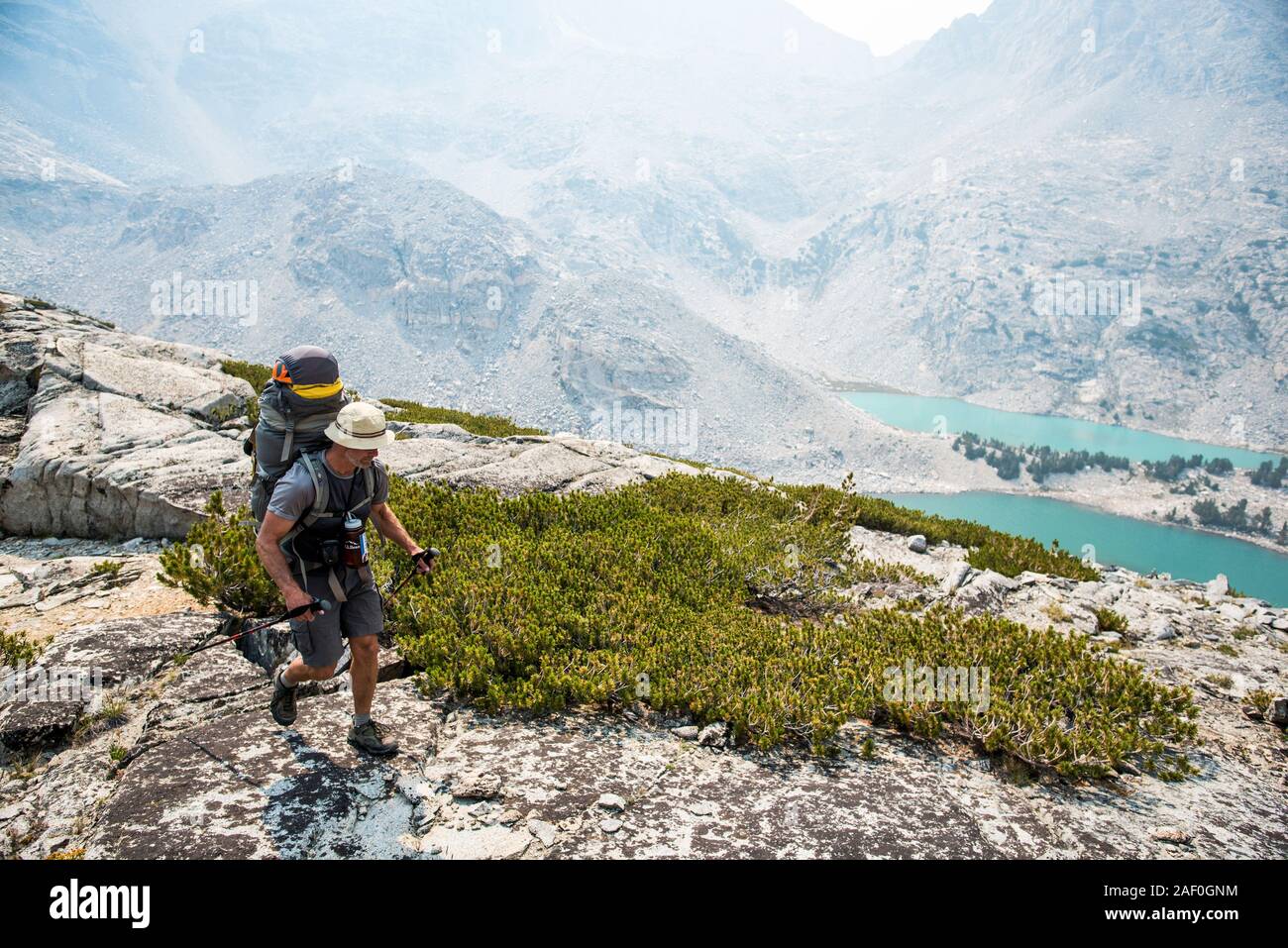 Man hiking through mountains with lakes in the distance Stock Photo