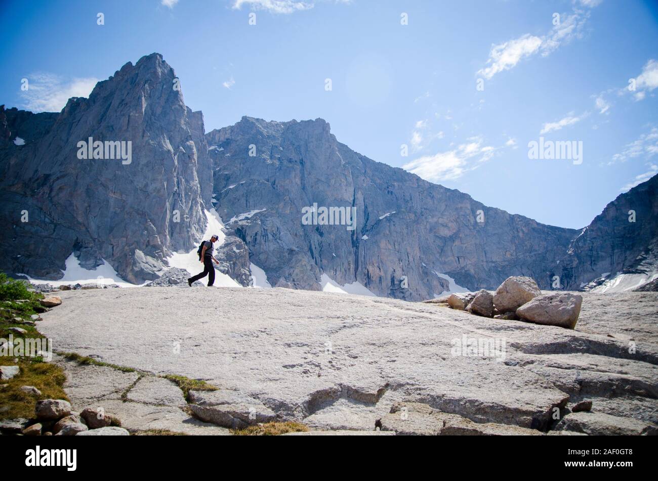 Man walking through the mountains with big cliffs behind Stock Photo